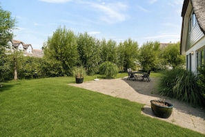 Ein gepflegter Garten mit einer Terrassenfläche, einem Esstisch und Stühlen.