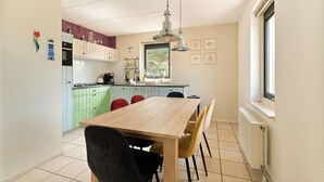 A modern kitchen with a wooden table and chairs, a window, and a view of greenery outside.