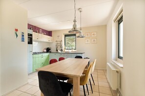 A modern kitchen with a wooden table and chairs, a window, and a view of greenery outside.