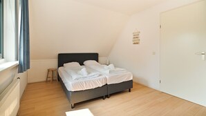 A bedroom with a bed, a small stool, a door, and a wall sign.