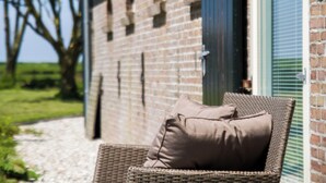 A wicker chair with a cushion outside a building with a brick facade and a window with blinds. - Beautiful apartment in an authentic Stolp farmhouse (Schagen)