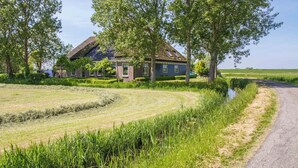 A rural house with a thatched roof, surrounded by lush greenery and a narrow road. - Beautiful apartment in an authentic Stolp farmhouse (Schagen)