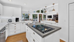 A modern kitchen with white cabinetry, a central island with a stovetop, and pendant lighting.