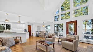 A spacious living area with a sofa, armchairs, a coffee table, and a kitchen in the background.