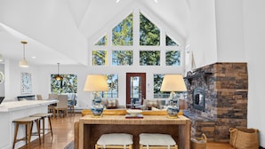 A spacious kitchen with a stone fireplace, large windows, and a high ceiling.
