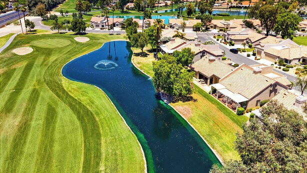 Un parcours de golf agrémenté d’un plan d’eau, entouré de bâtiments résidentiels et dominé par un paysage montagneux.
