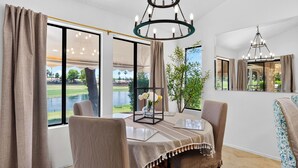 Un espace repas comprenant une table, des chaises, un lustre et donnant sur un terrain de golf.