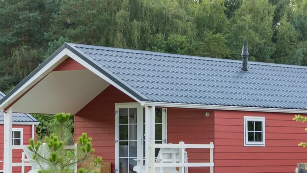 Een rode houten hut met een overdekte veranda en schoorsteen.