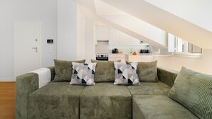 A modern living room with a green sofa, geometric pillows, and a kitchen in the background. - Comfortable Family Apartment in Central Lisbon (Lisbon)