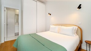 A bedroom with a bed, a green blanket, a wooden headboard, a nightstand, and a wall-mounted light fixture. - Comfortable Family Apartment in Central Lisbon (Lisbon)