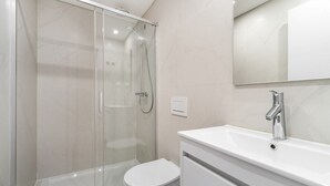 A modern bathroom with a glass-enclosed shower, a white toilet, and a sink with a mirror above it. - Comfortable Family Apartment in Central Lisbon (Lisbon)