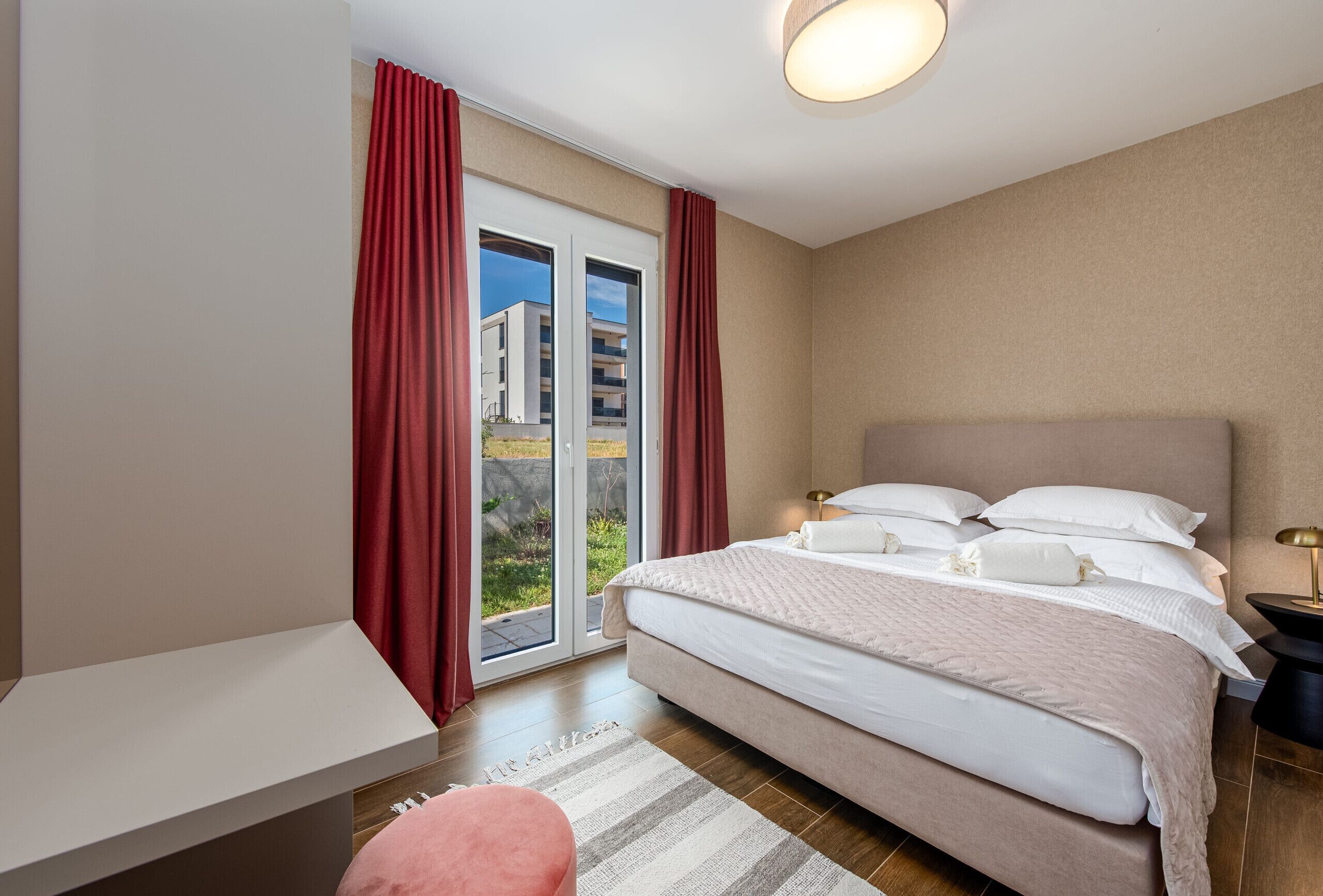 A bedroom with a bed, a desk, a chair, a nightstand, and a view through a sliding door.