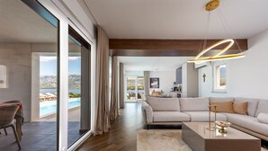 A modern living room with a large sofa, a coffee table, and a view of a pool and mountains. - Villa Wave of Love ZadarVillas (Rovanjska)