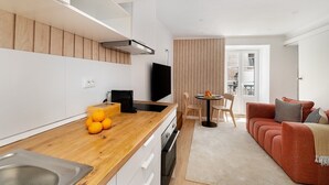 Uma cozinha moderna com bancada de madeira, forno embutido e televisão. Há uma área de jantar com mesa e cadeiras, e um sofá vermelho na sala de estar.