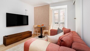 Uma sala de estar moderna com televisão de tela plana, um armário de madeira, um sofá e uma área de jantar com mesa e cadeiras.