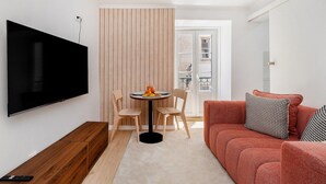 Uma sala de estar moderna com uma televisão de tela plana, uma mesa redonda com cadeiras, um sofá vermelho e um painel de madeira.