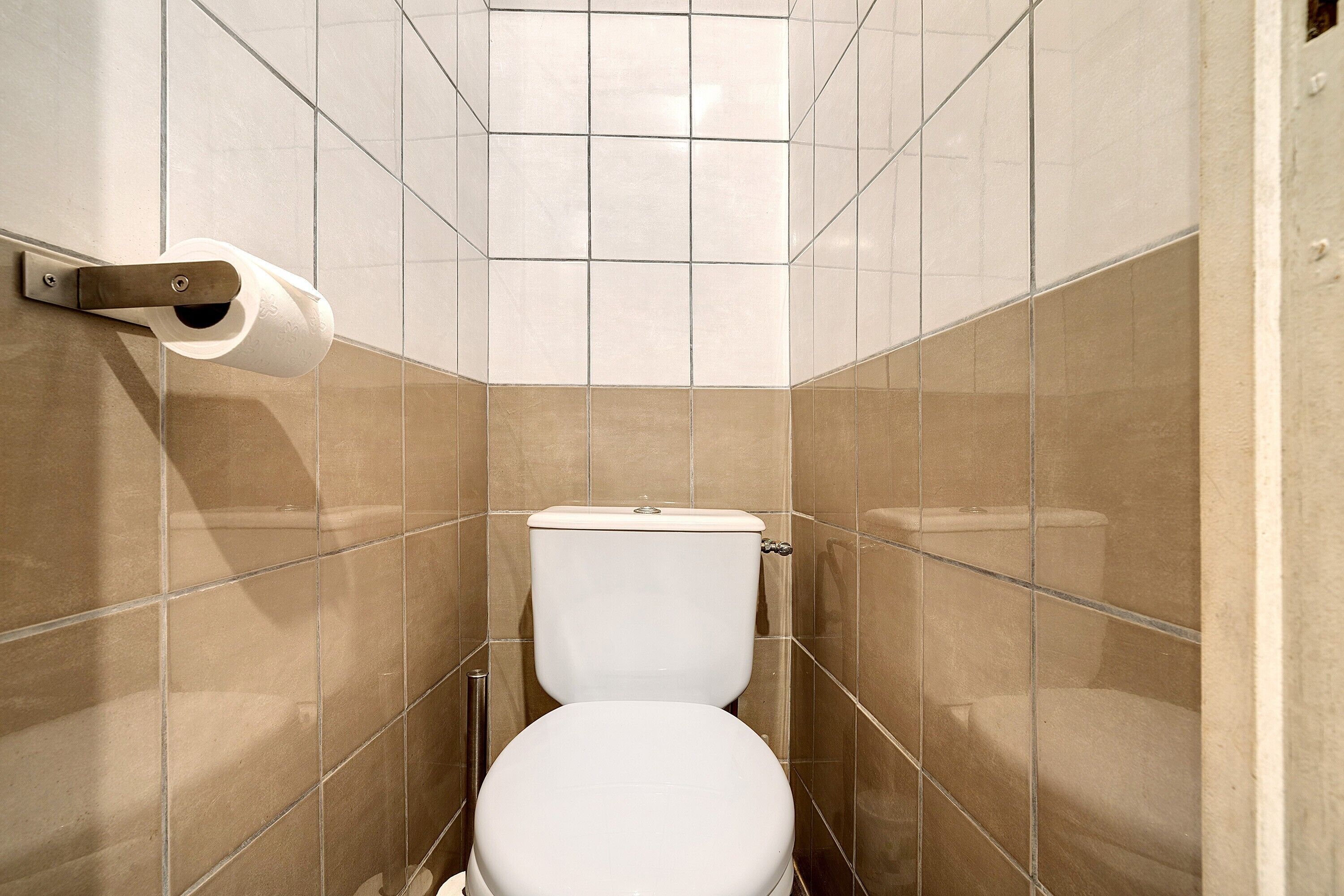 A bathroom with a toilet, a toilet paper holder, and tiled walls.
