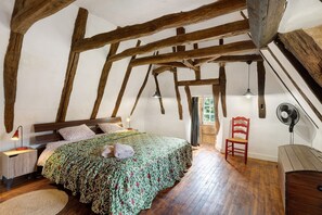 Slaapkamer met zichtbare houten balken, een bed met bloemenbeddengoed, een nachtkastje, een stoel en een bureau.