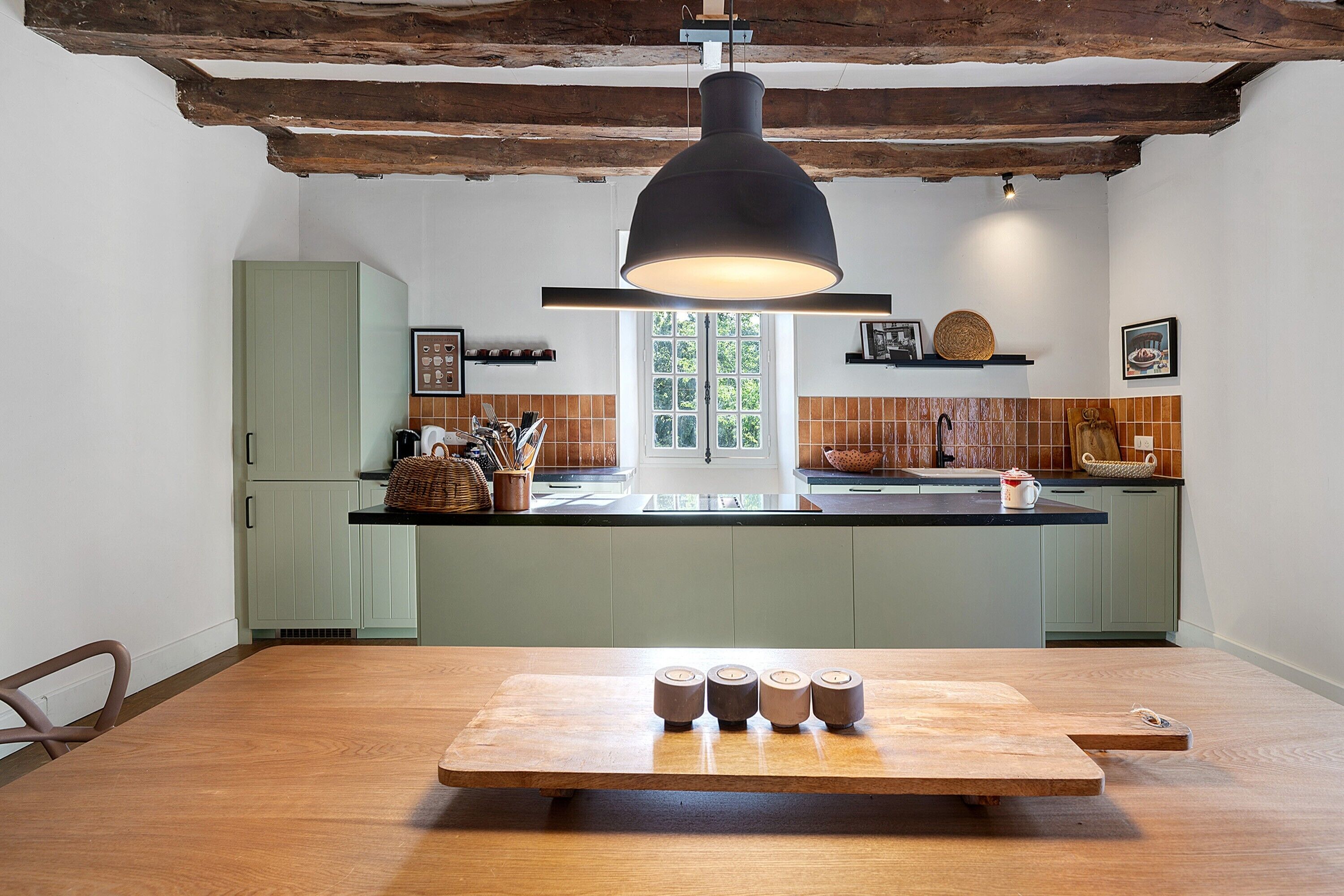 Una cucina con tavolo in legno, lampada a sospensione e finestra vista su vegetazione.