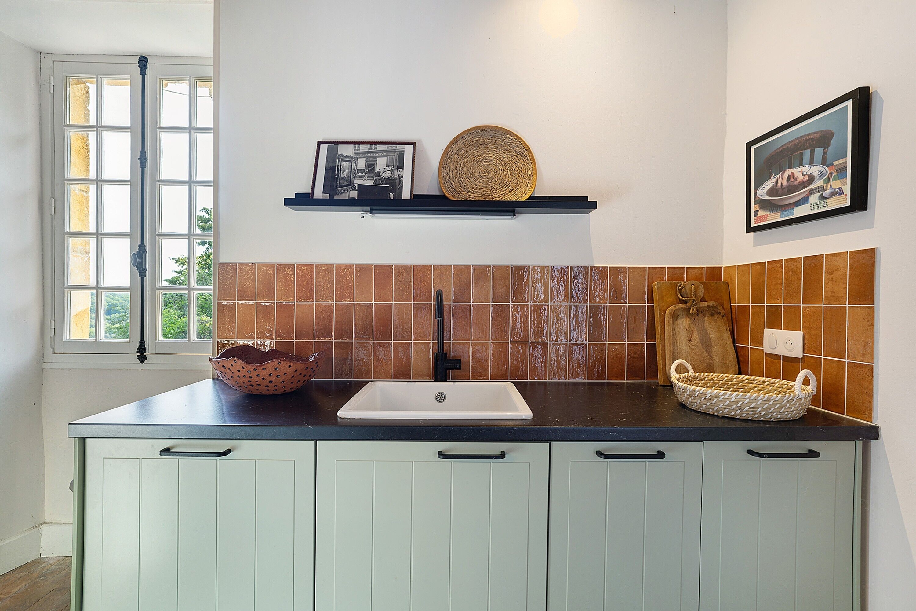 A kitchen with a window, a sink, a shelf with decorative items, and a tiled backsplash.