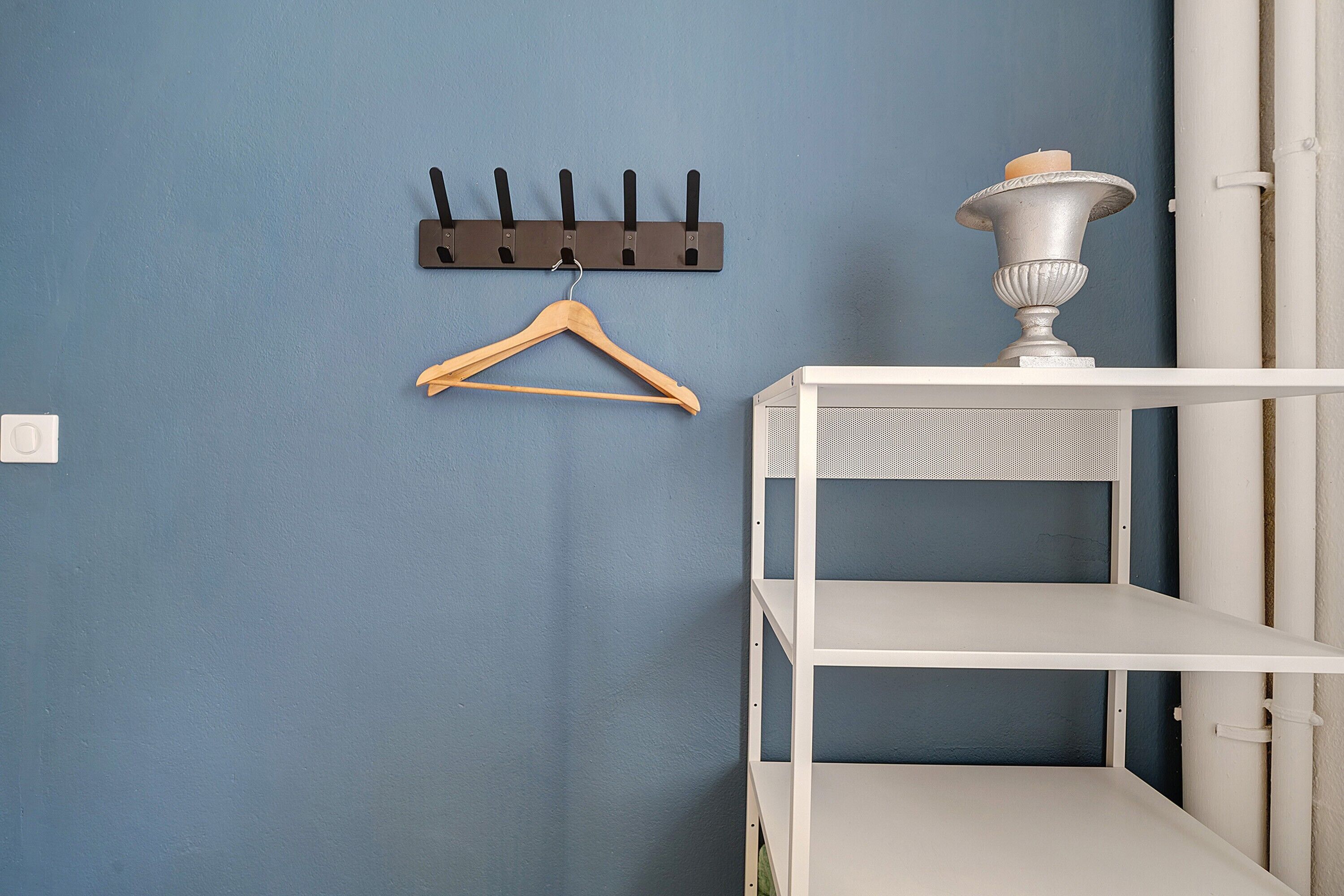 Una habitación con pared azul, un perchero de madera, un estante blanco y un objeto decorativo de metal.