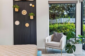 A modern bedroom with a bed, a chair, a large window, and a wall with vertical stripes and decorative items. - South Austin Retreat • Pool + Fire Pit • Near South Congress | Oaklane Zen (Austin)