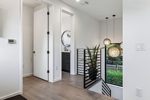 A modern interior with a wooden floor, a staircase with a black railing, and a view of greenery through a window. - South Austin Retreat • Pool + Fire Pit • Near South Congress | Oaklane Zen (Austin)