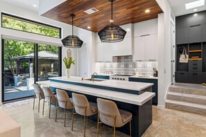 A modern kitchen with a central island, bar stools, pendant lighting, and a view of the outdoors. - South Austin Retreat • Pool + Fire Pit • Near South Congress | Oaklane Zen (Austin)
