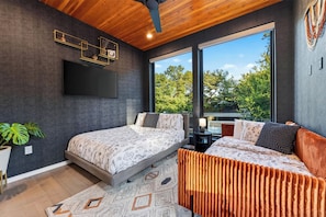 A modern bedroom with a bed, a sofa, a TV, and a large window. - South Austin Retreat • Pool + Fire Pit • Near South Congress | Oaklane Zen (Austin)