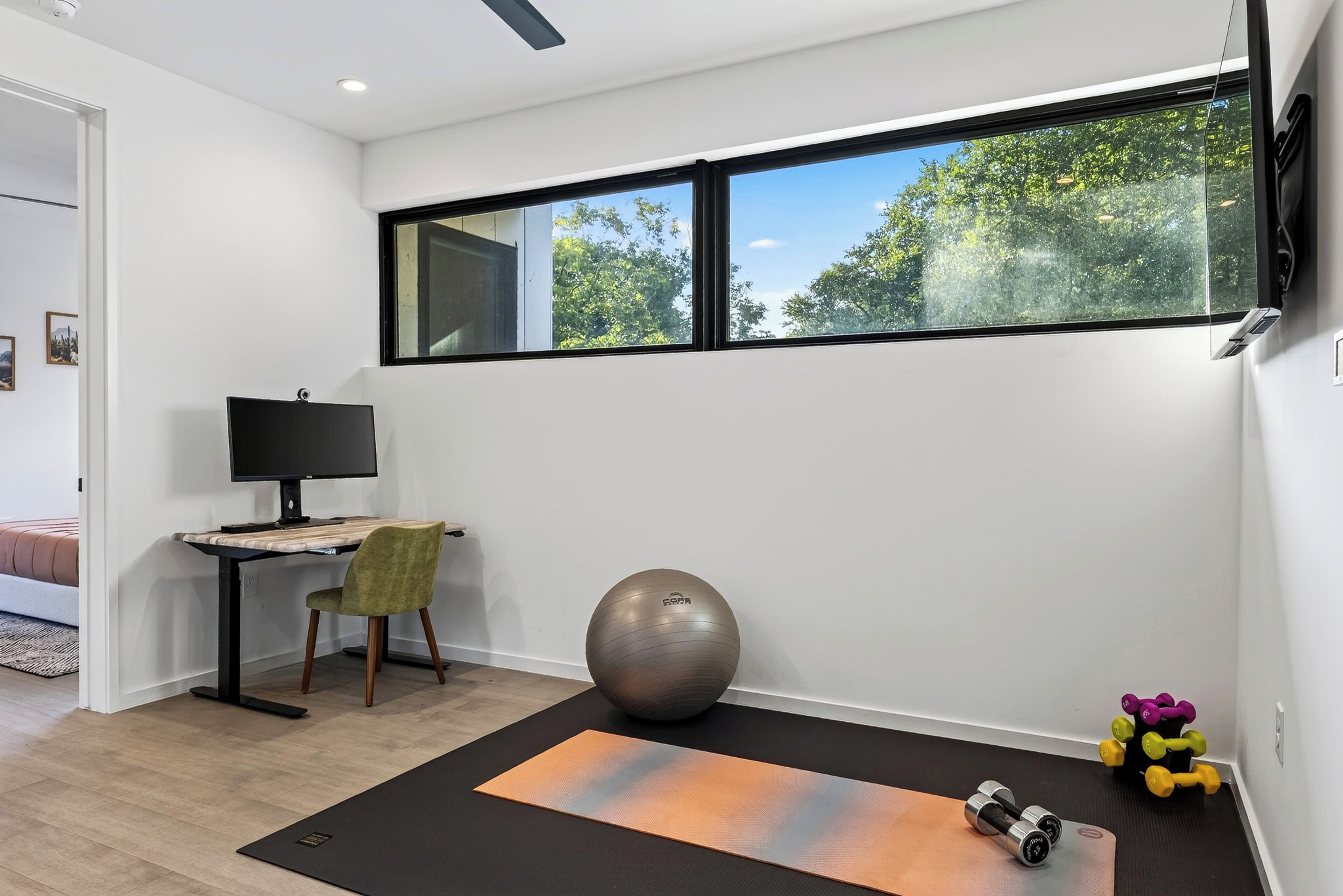 A modern room with a desk, chair, exercise ball, yoga mat, and dumbbells.
