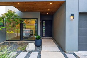 A modern building entrance with a wooden ceiling, glass doors, and a potted plant. - South Austin Retreat • Pool + Fire Pit • Near South Congress | Oaklane Zen (Austin)
