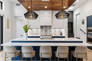 A modern kitchen with a central island, bar stools, pendant lighting, and a backsplash with a speckled pattern. - South Austin Retreat • Pool + Fire Pit • Near South Congress | Oaklane Zen (Austin)