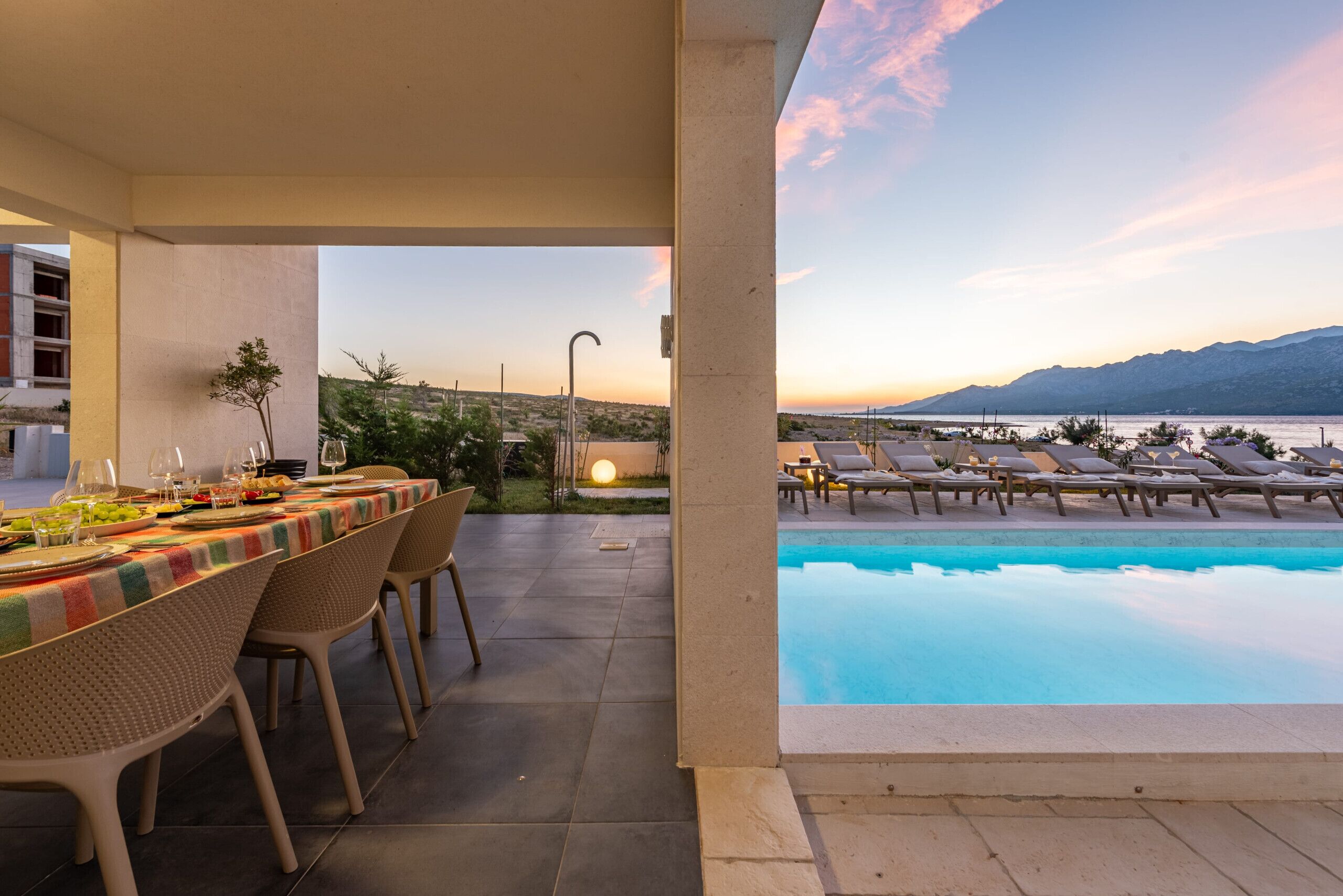 Un área de comedor al aire libre con vistas a una piscina y montañas.