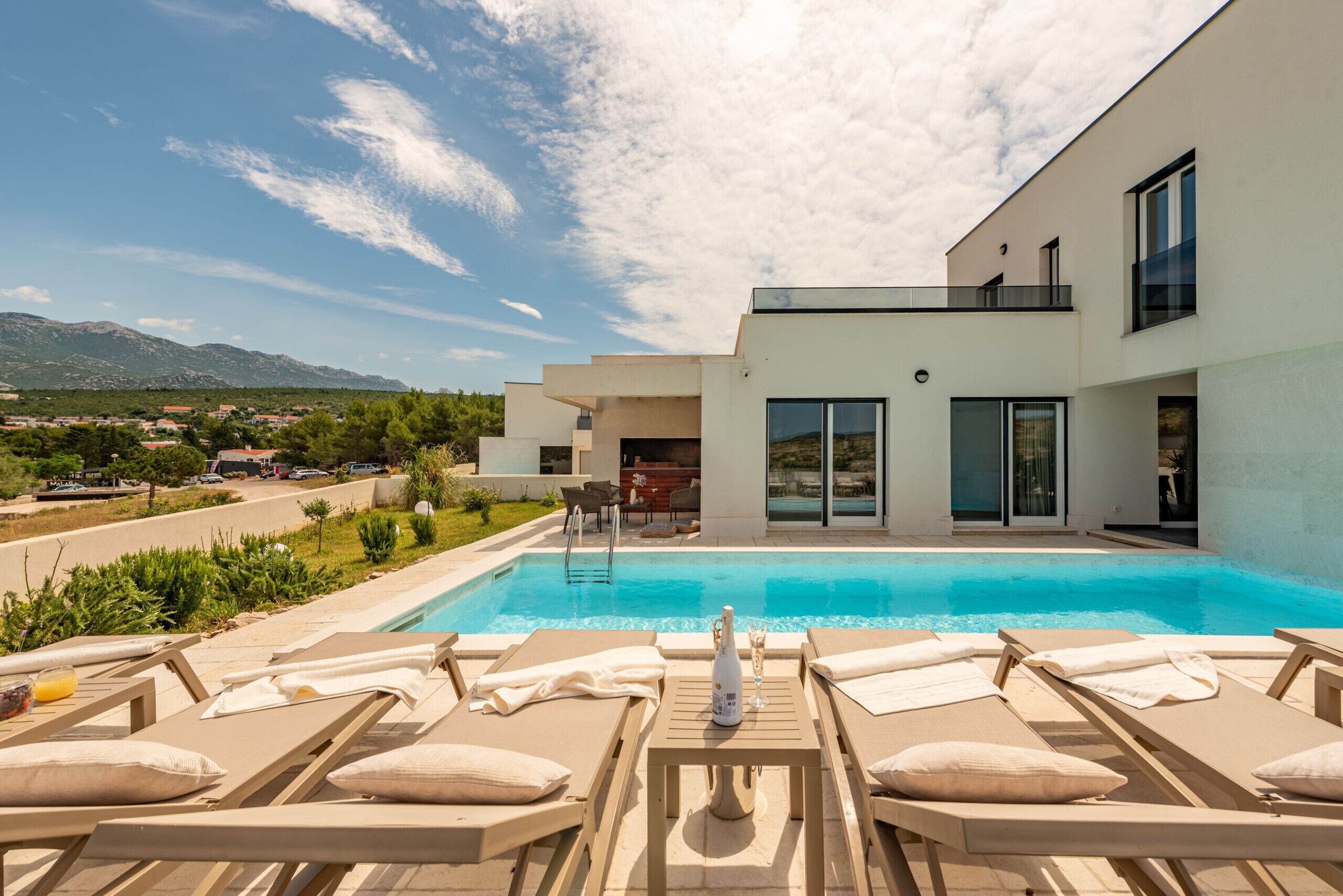A modern poolside area with lounge chairs, a pool, and a view of the mountains.