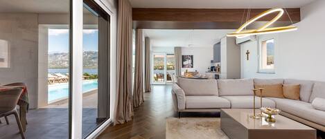 A modern living room with a large sofa, a coffee table, and a view of a pool and mountains.
