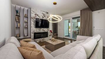 Un salon moderne avec un canapé, un téléviseur à écran plat, une cheminée et un luminaire au plafond.