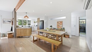 Une cuisine spacieuse avec un îlot central, une table à manger en bois et un banc, de grandes fenêtres et un luminaire suspendu.