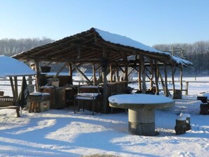 A rustic wooden structure with a snow-covered roof, a stone table, and a snow-covered mushroom. - defaultName (Penzlin)