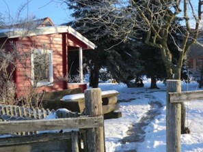 A red wooden building with a porch, surrounded by snow-covered ground and trees. - defaultName (Penzlin)