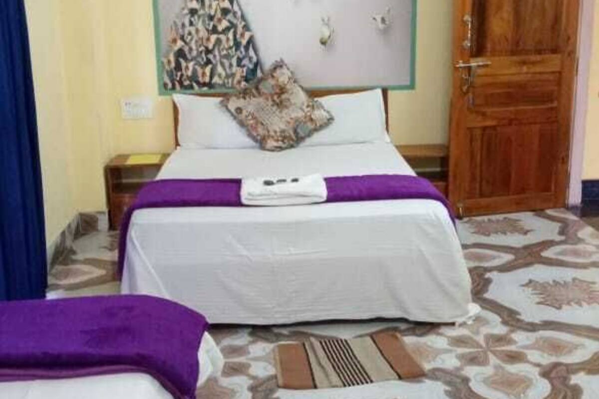 Quarto de hotel com duas camas, piso estampado, aparelho de ar condicionado e porta de madeira.