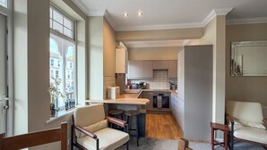 A modern kitchen with a built-in oven, a dining area with two chairs, and a view of the street through a window. - Louisa Bay - UK51814 (Broadstairs)