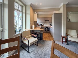 Een moderne keuken met een ingebouwde oven, een eethoek met twee stoelen en uitzicht op de straat door een raam.