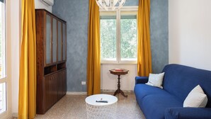 Una habitación con sofá azul, armario de madera, una pequeña mesa redonda y una ventana con cortinas amarillas.