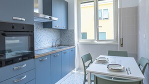 Una cocina moderna con armarios azules, un horno empotrado y un comedor con una mesa dispuesta para dos personas.