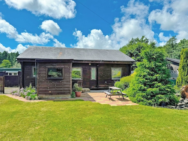 Une cabane en bois avec un porche, un petit jardin et un ciel bleu dégagé.