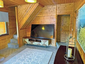 L’intérieur d’un chalet en bois, avec une télévision, un escalier, un tapis et un chandelier.