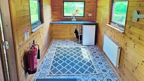 A small, wooden cabin with a kitchenette, a window with a view of greenery, and a fire extinguisher mounted on the wall. - 2 bedroom accommodation in Ellerbeck (Ellerbeck)