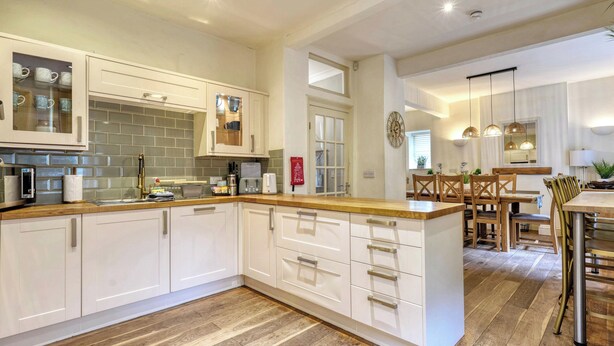 Una cocina moderna con armarios blancos, una encimera de madera y un comedor con mesa y sillas de madera.