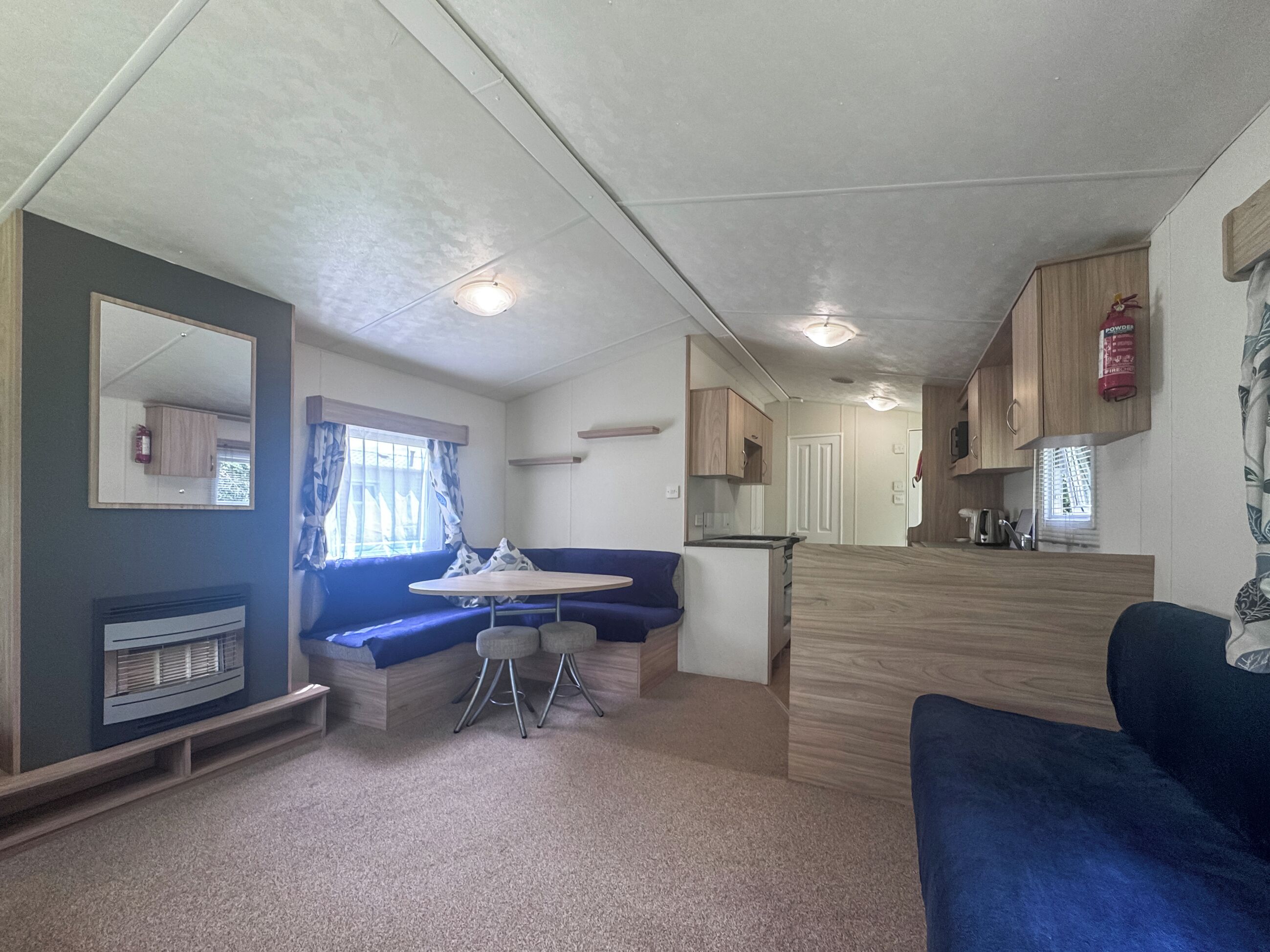 A compact RV interior with a kitchenette, a seating area with a table and chairs, and a large mirror.
