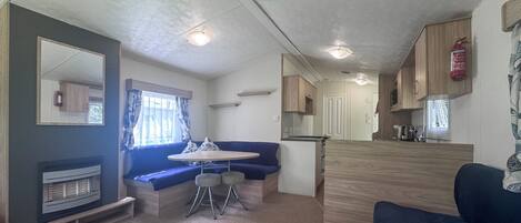 A compact RV interior with a kitchenette, a seating area with a table and chairs, and a large mirror.